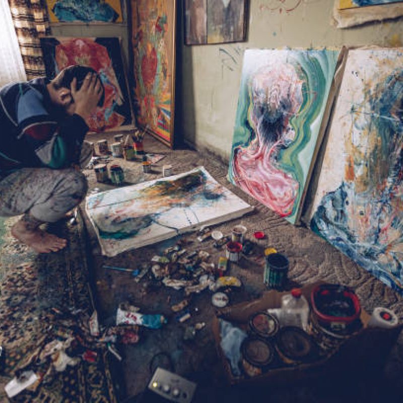 Artist Painter Working On Painting In Studio With Art Supplies Around Him