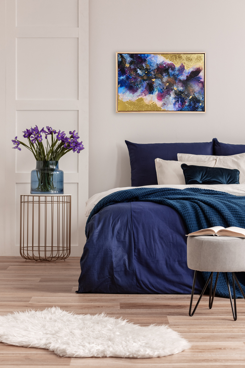 Purple Flowers In Blue Glass Vase On Stylish Bedside Table Next To King Size Bed