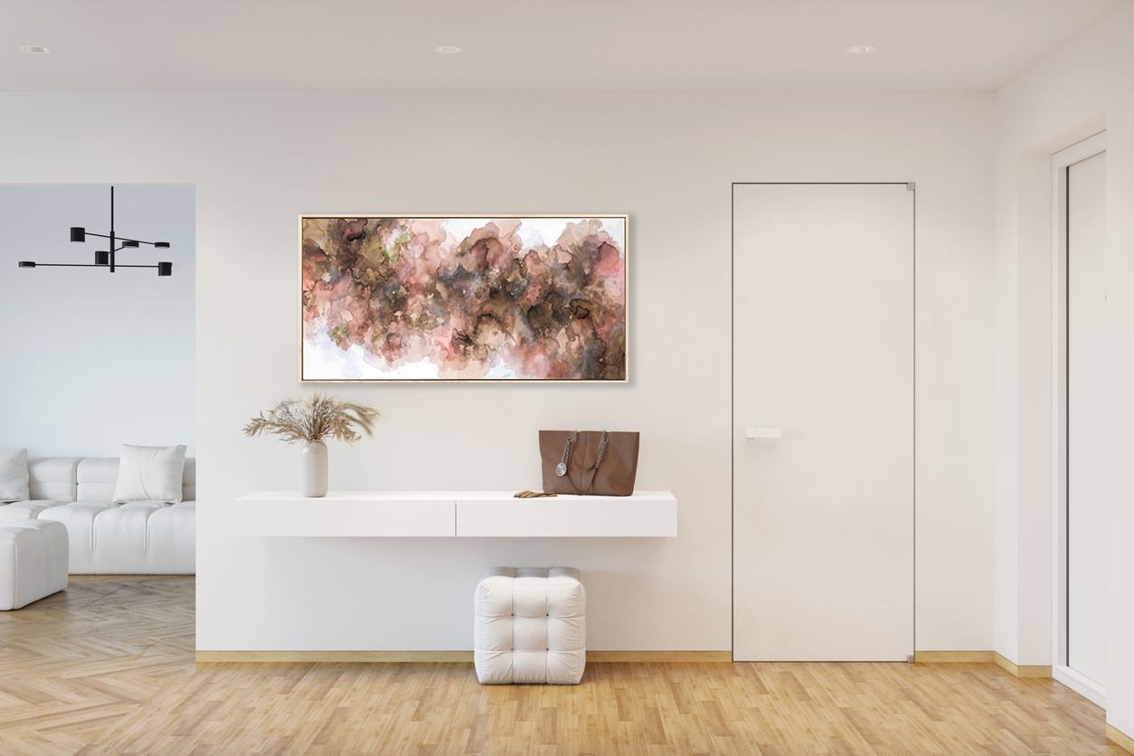 A White Entrance Hallway With A Blank Horizontal Poster Above A Cabinet With The Pampas Grass In A Vase, A Pouf On A Parquet Floor, Two Doors, A Doorway To The Living Room With A White Sofa.